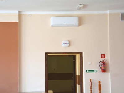 Zamontowany klimatyzator marki Hisense nad wejściem po prawej stronie od wejścia widać gaśnice i oznaczenia wyjście.